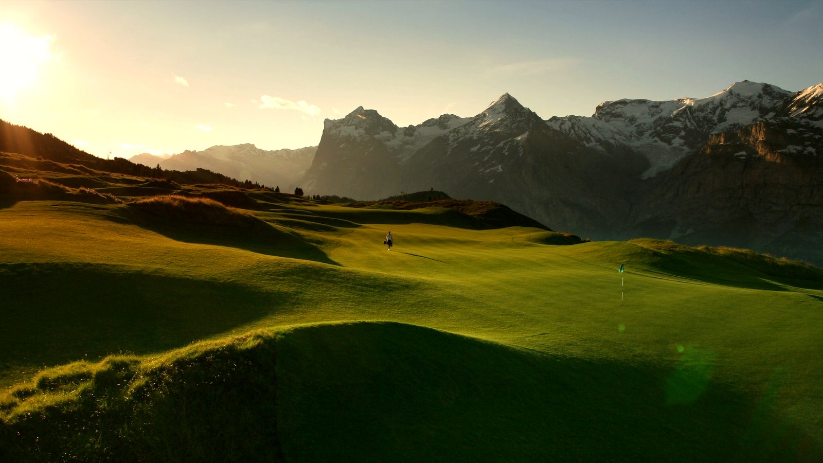 A pristine alpine golf course framed by snow-capped peaks in summer
