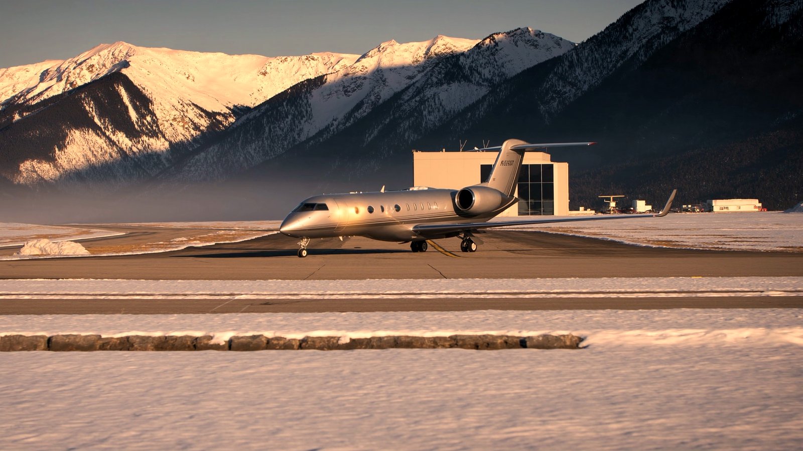 A private jet on a snowy alpine runway with mountains behind at golden hour